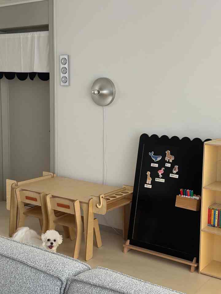 ベージュのナチュラルカラーの子供部屋、二人用の木製子供机と黒板、小さな白い犬がいる温かみのある空間