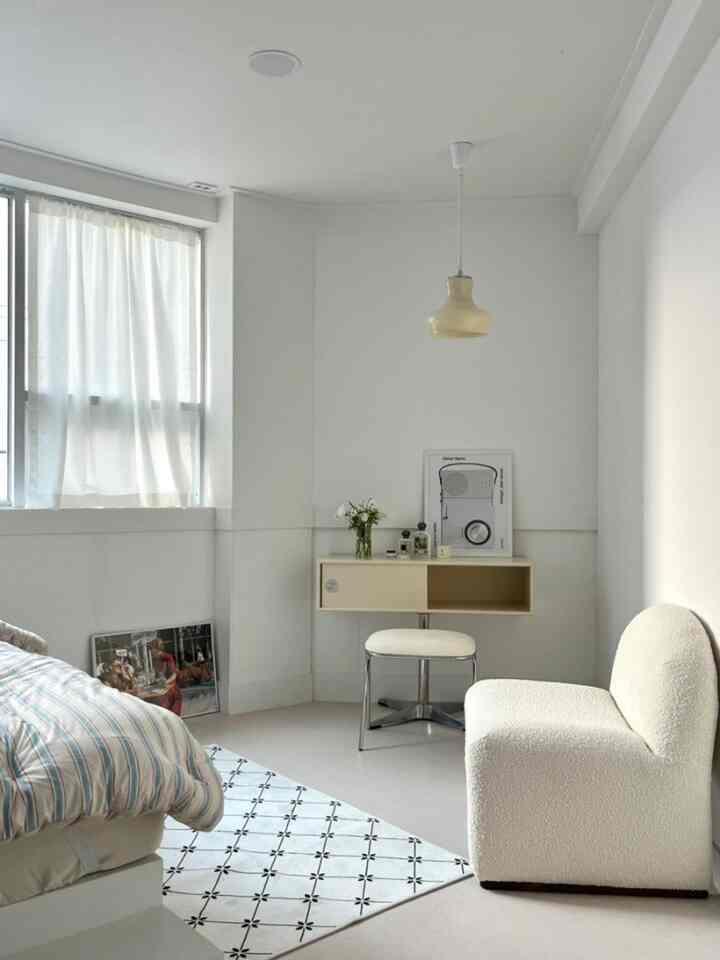 Minimal bedroom in white and beige tones featuring a sofa, stool, and wall-mounted console for a clean look