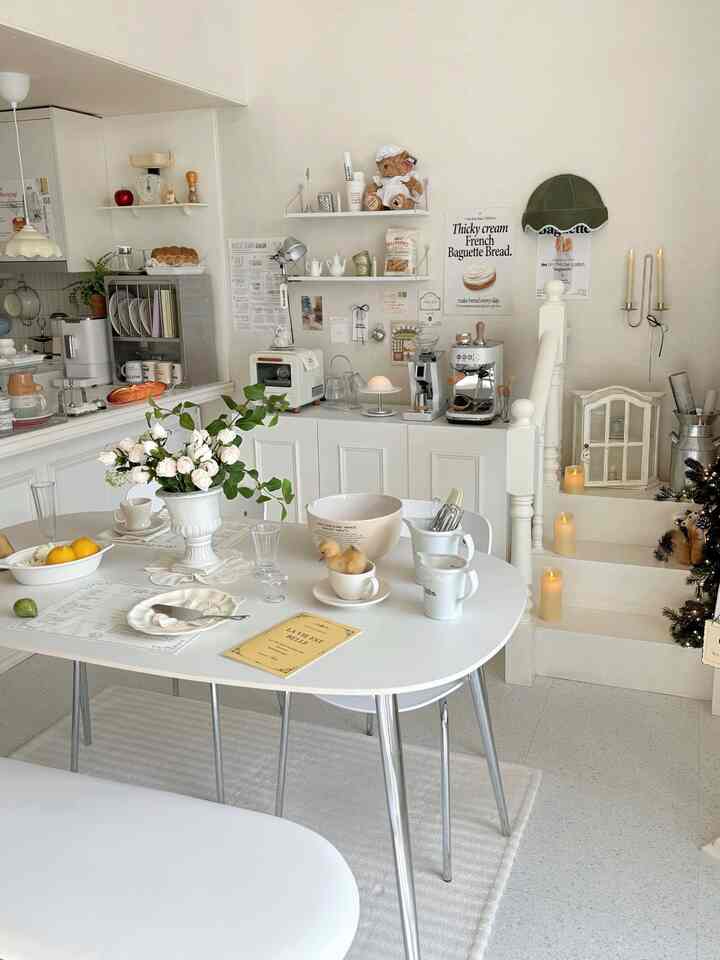 クリーム色と白色を基調としたフレンチカントリースタイルのキッチンとダイニングルーム、中央にテーブルとベンチが配置された温かみのあるインテリア