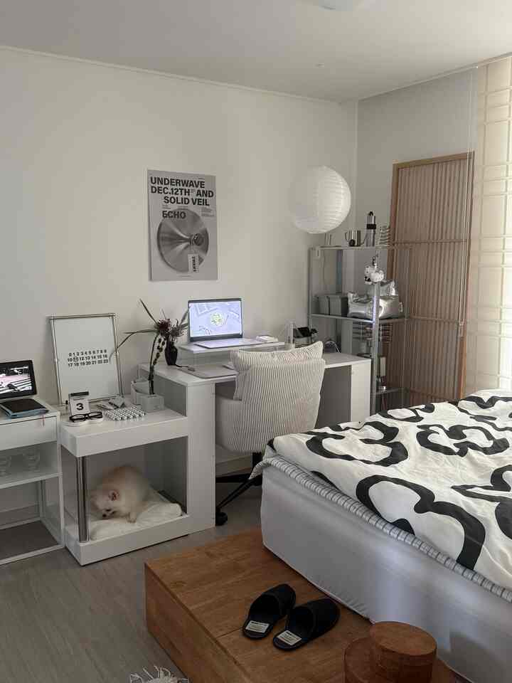 白を基調とした寝室、シンプルなデスクとチェアが配置されたコンパクトなワークスペースと小さなペットがいる落ち着いたインテリア