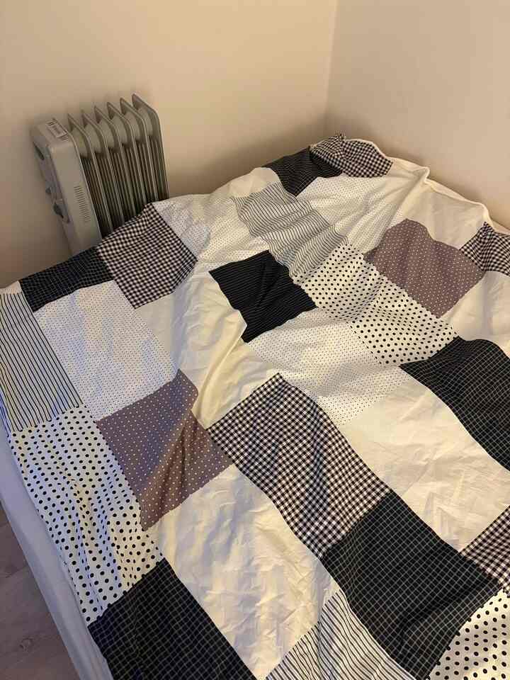 白と黒のトーンの寝室、中央にパターンのブランケットが敷かれたベッドが置かれた落ち着いた空間