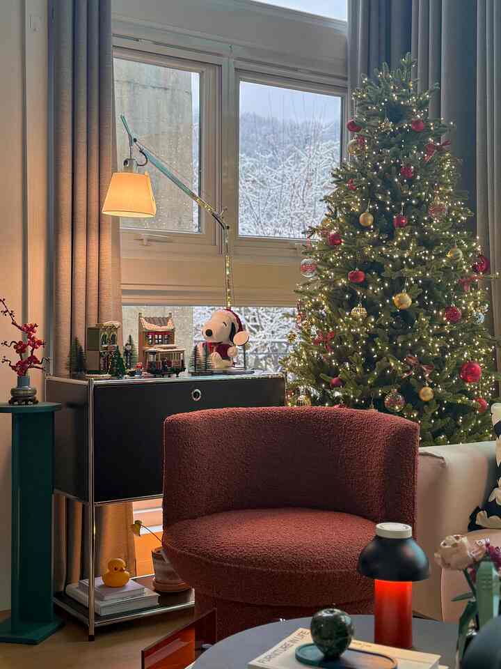 A warm living room featuring a red armchair and a Christmas tree adorned with red and gold ornaments and twinkling lights