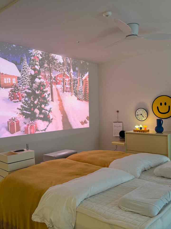 White walls and ceiling, yellow bedding, and modern furniture in a bedroom with home cinema setup