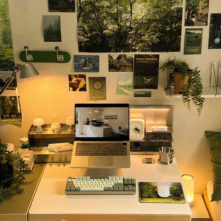 White and green toned home office featuring a desk with laptop, keyboard, plants, and cozy lighting
