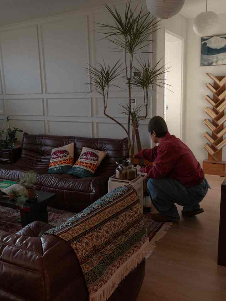 ブラウンレザーソファとエスニック柄カーペットが配置されたナチュラルトーンのリビング、オバン暖炉の上にやかんが置かれた雰囲気のある空間