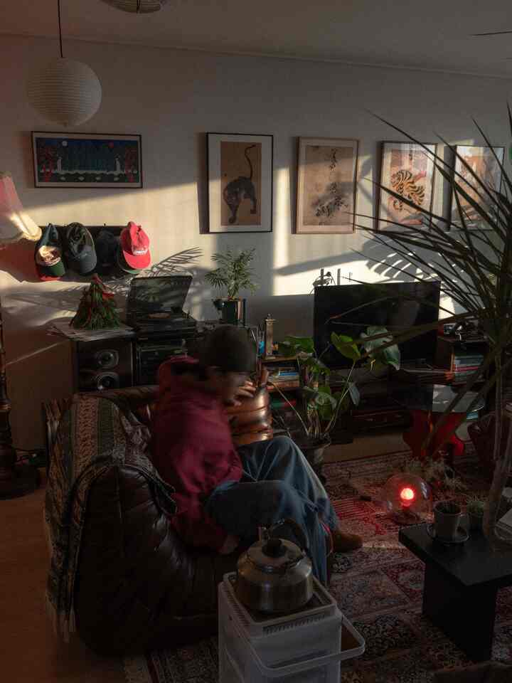 ヴィンテージとナチュラルな色調のリビング、レザーソファとフロアランプ、多様な絵画と植物が配置された雰囲気ある空間