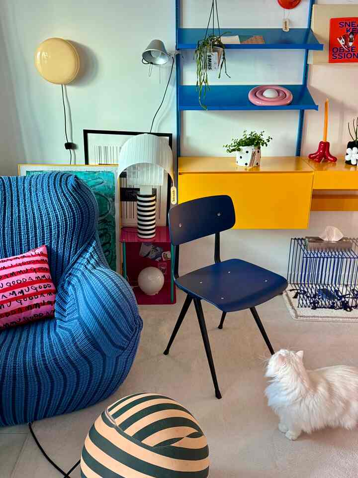 A blue and yellow toned single household dining space featuring a blue sofa, chair, wall sconces, and a cat for a cozy atmosphere