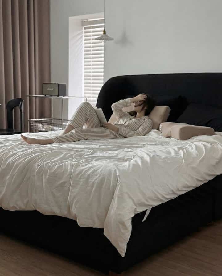 白と黒のトーンの寝室、中央に大きなベッドと枕が配置されており、居心地の良い雰囲気のインテリア