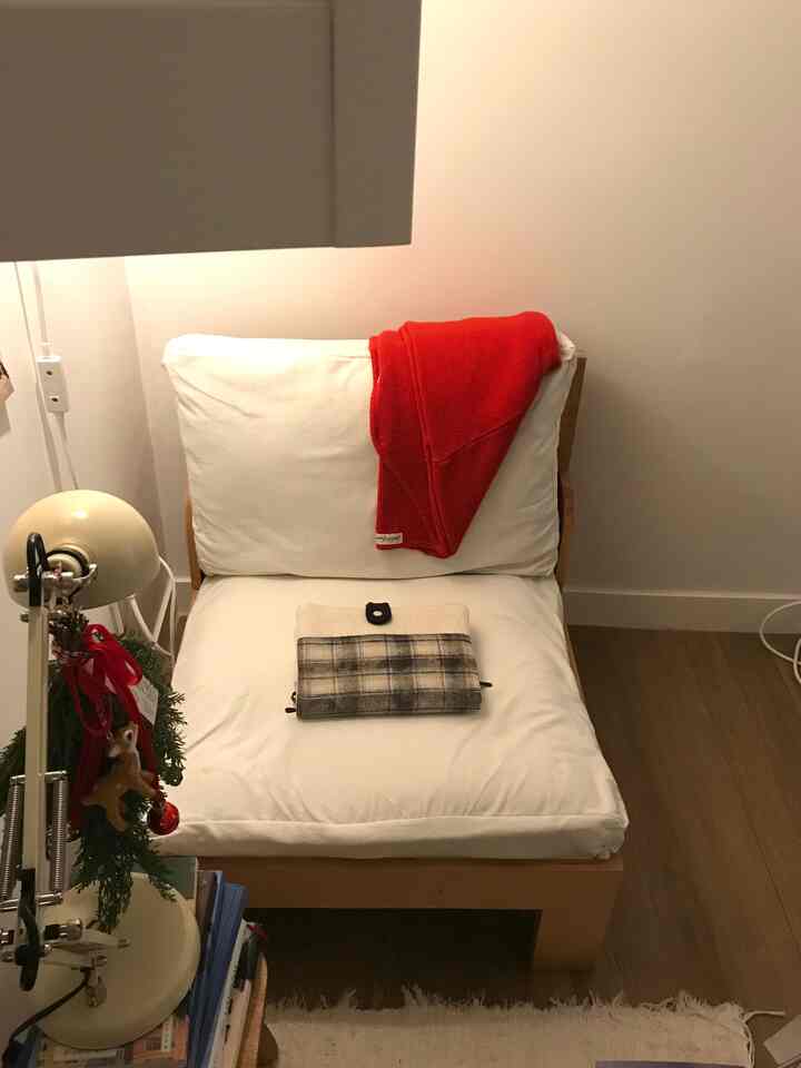 温かみのあるホワイトと木目調の一人暮らし用リビング、ソファと赤いブランケット、テーブルランプが配置された雰囲気のあるインテリア