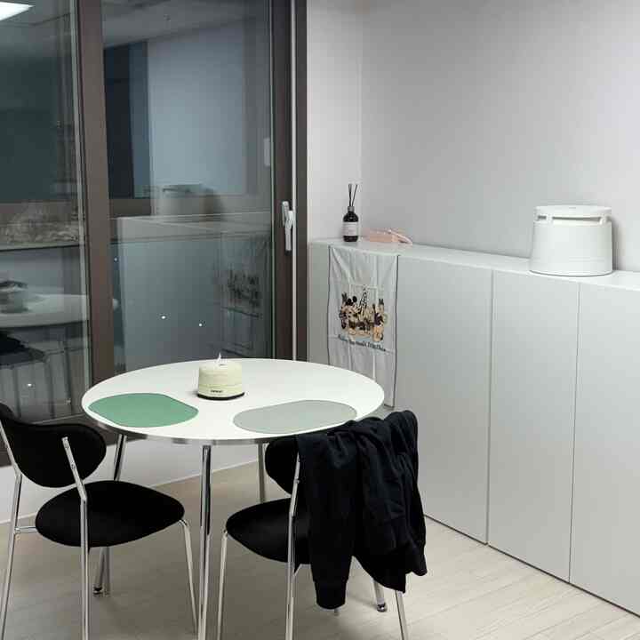 白とナチュラルカラーの小さな食事兼作業スペース、丸いテーブルと黒い椅子が配置された整った2人用ダイニングルーム