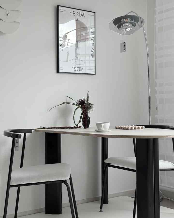 ホワイトとブラックのトーンのダイニング、ミッドセンチュリーモダンスタイルのポスターとフロアランプが配置されたシンプルでモダンな雰囲気のインテリア
