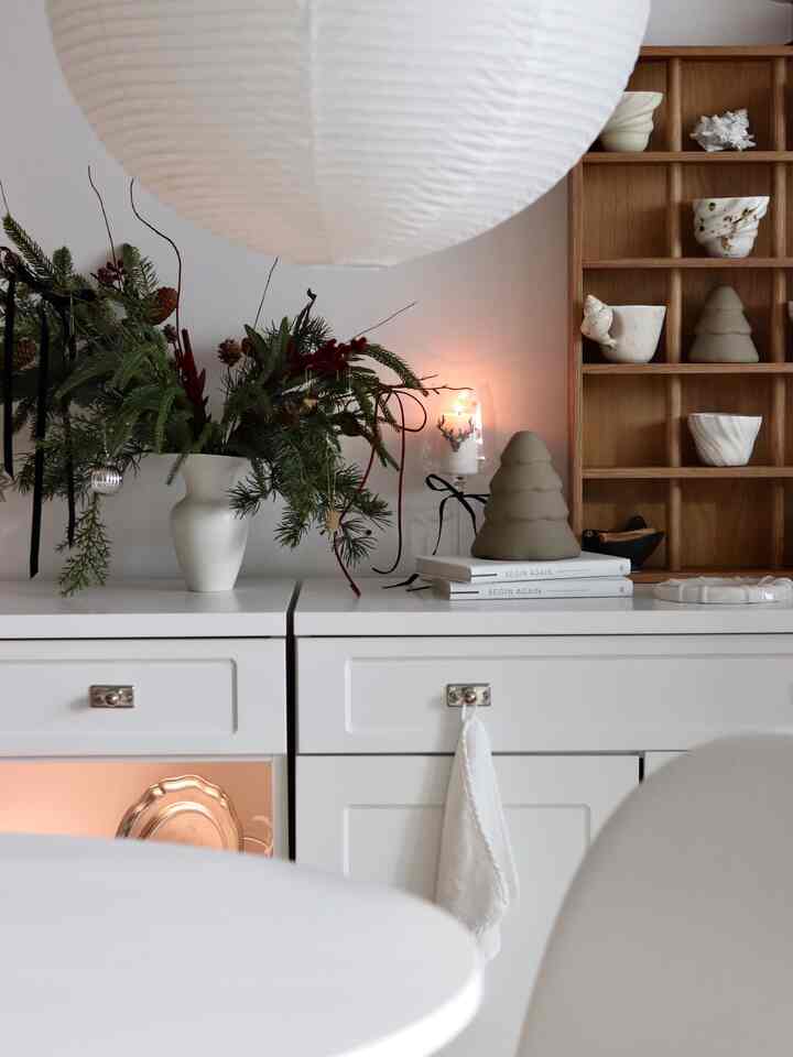 ホワイトとウッドトーンのリビングルーム、白いキャビネットの上に植物とキャンドルが温かみのある雰囲気を醸し出すインテリア