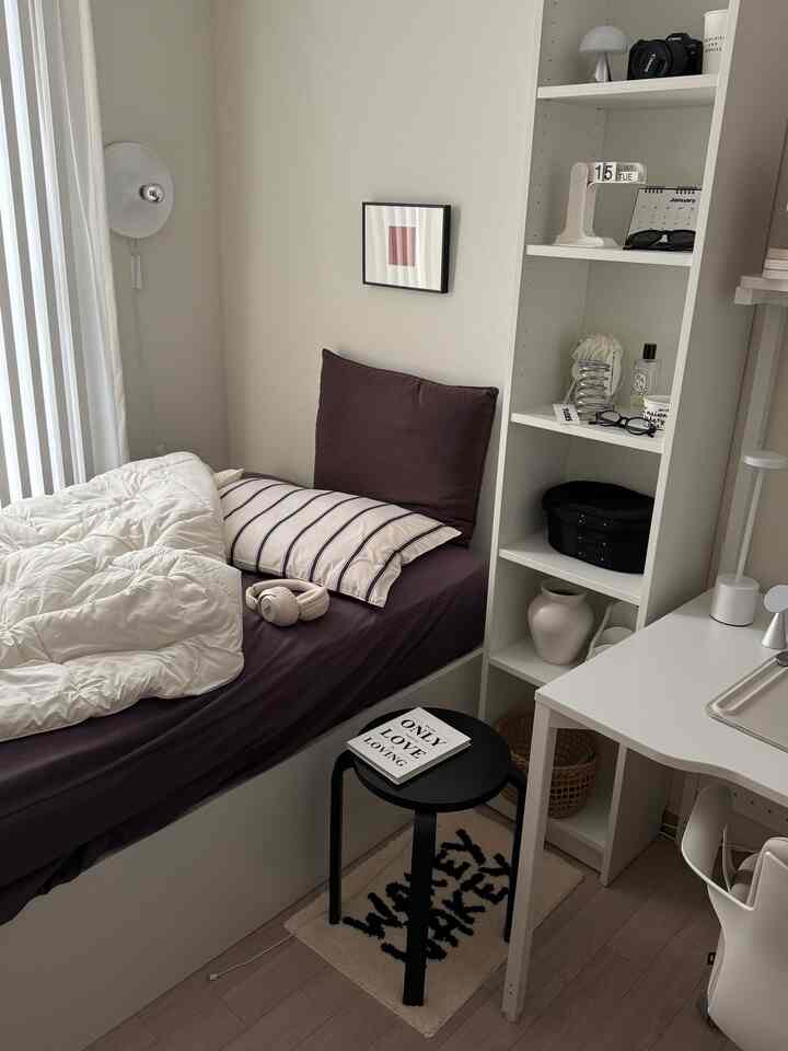 ブラウンとホワイトのトーンのワンルーム寝室、清潔な寝具と本棚が配置された雰囲気のあるインテリア