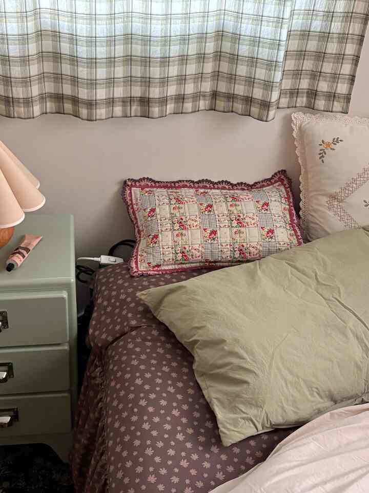 ヴィンテージ風パッチワーククッションとグリーンのベッドカバーが調和した寝室、チェック柄カーテンとレースクッションが居心地の良い雰囲気を演出する空間