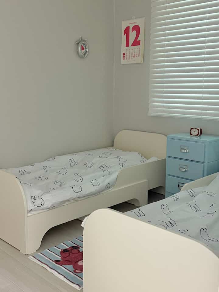 白とベージュの色調の子供部屋、2つの子供用ベッドとパステルカラーのキャビネットが配置された雰囲気のあるインテリア