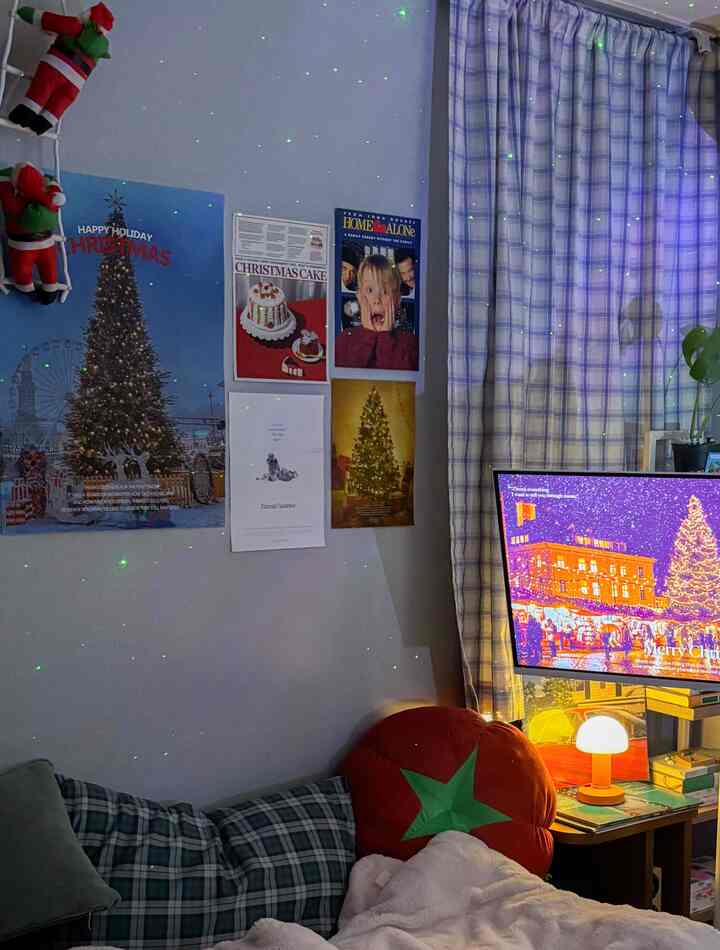 青みがかった壁とカーテンのワンルーム寝室、壁にはクリスマステーマのヴィンテージポスターとサンタのぬいぐるみが配置された雰囲気のある空間
