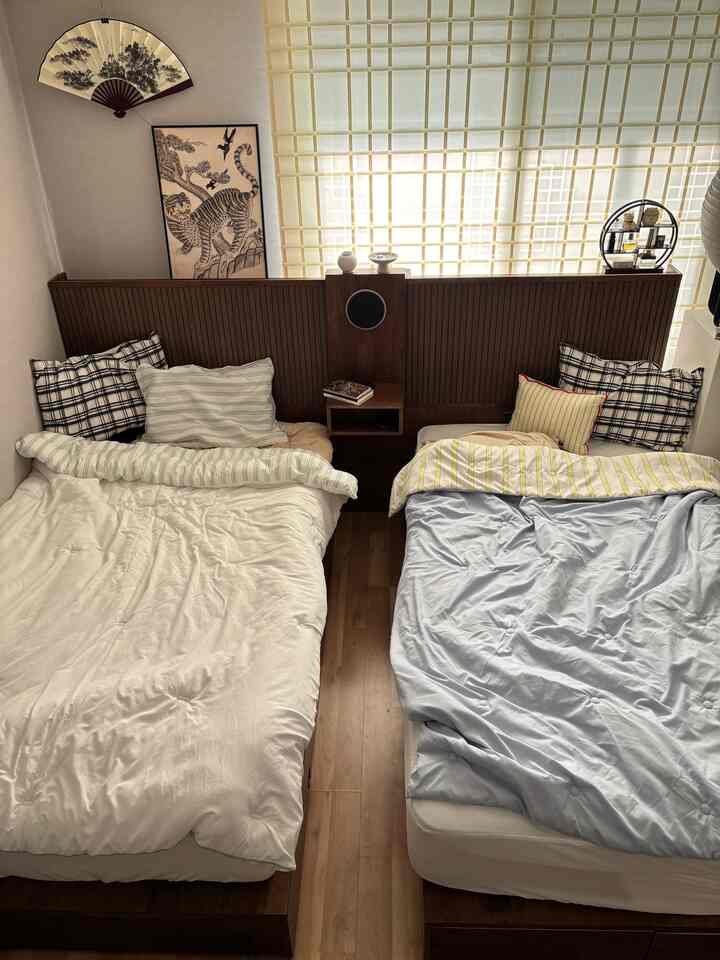 ナチュラルな木目調とベージュ色調の寝室、中央にスライド式のナイトテーブルで仕切られたツインベッドが配された落ち着いた空間