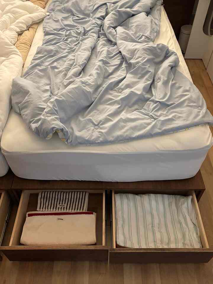 ナチュラルカラーの寝室、収納引き出し付きのベッドと季節の変わり目の布団が配置された清潔感のあるインテリア