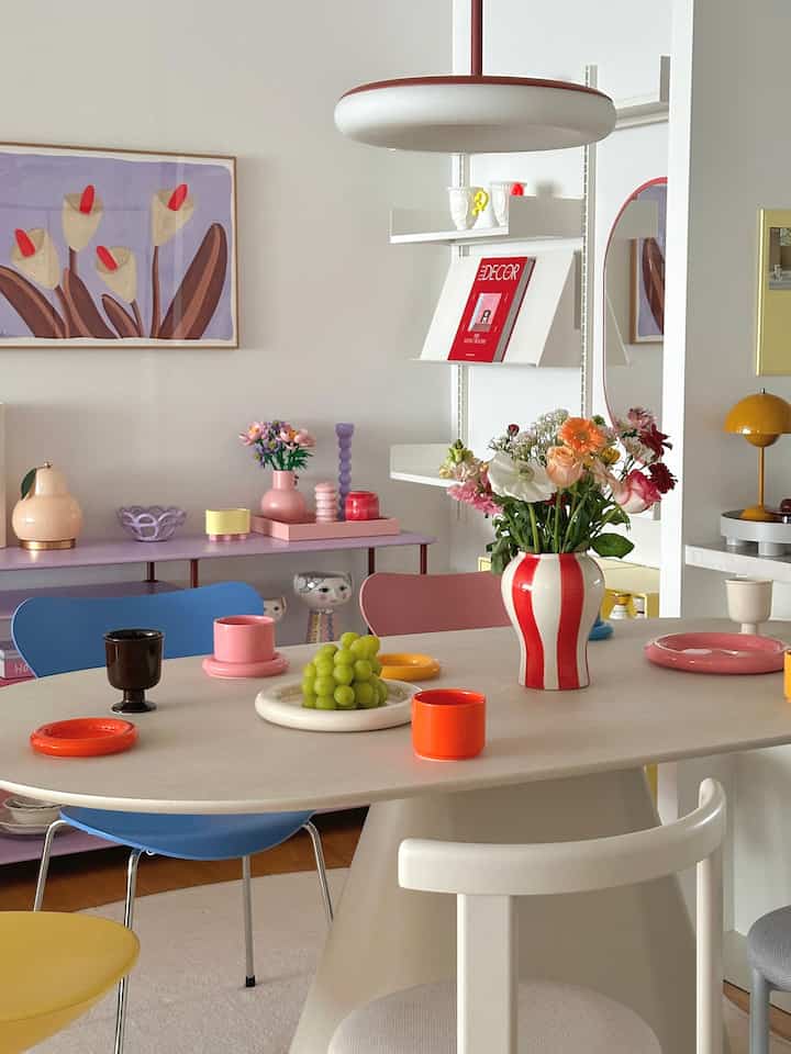 白い壁とパステルカラーの家具、赤いストライプの花瓶とペンダントライトが配置されたカフェ風のダイニングルーム