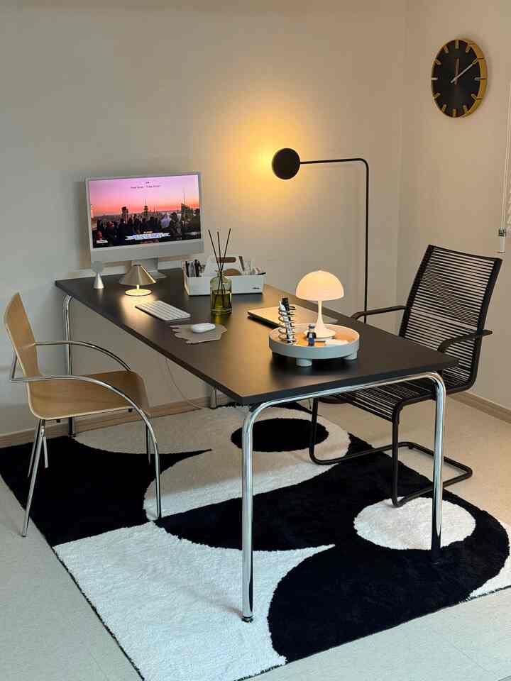 白と黒のトーンの書斎、黒いデスクと椅子、白黒の模様のラグが配置されたモダンなインテリア