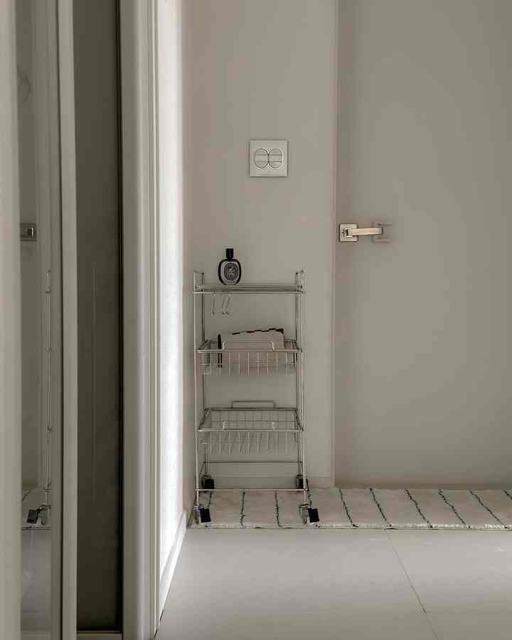 白色の狭いバスルーム前スペースにシルバーの3段トロリーが配置され、タオルが整頓された清潔でモダンなインテリア