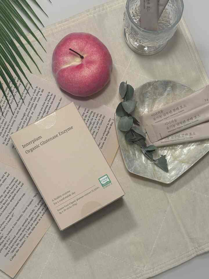 ナチュラルなベージュトーンのテーブル上、オーガニック酵素パッケージとシェルプレート、植物の葉が配置された落ち着いたおうちカフェの雰囲気のあるインテリア