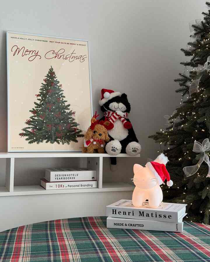 赤と緑のチェック柄テーブルマットがあるリビング、クリスマスツリーと猫型ムードランプ、クリスマスポスターで飾られた温かみのある雰囲気のインテリア