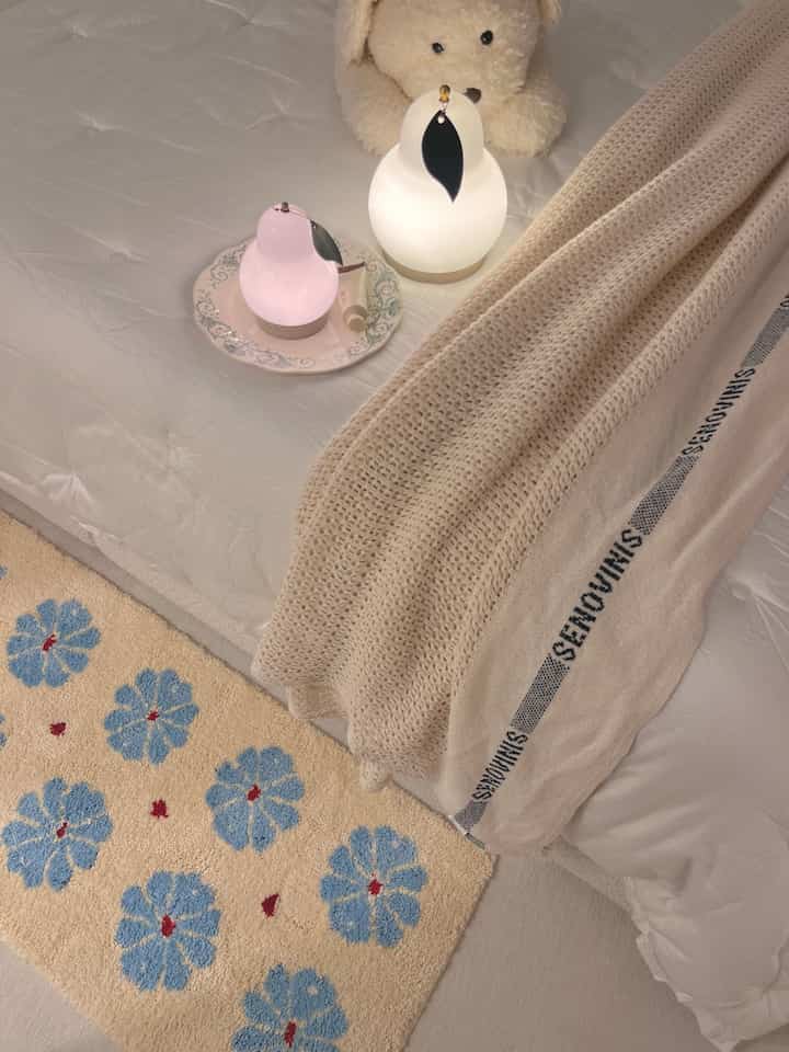Natural color bedroom featuring white bedding, beige throw blanket, cute stuffed toy, and soft table lamps creating a cozy atmosphere