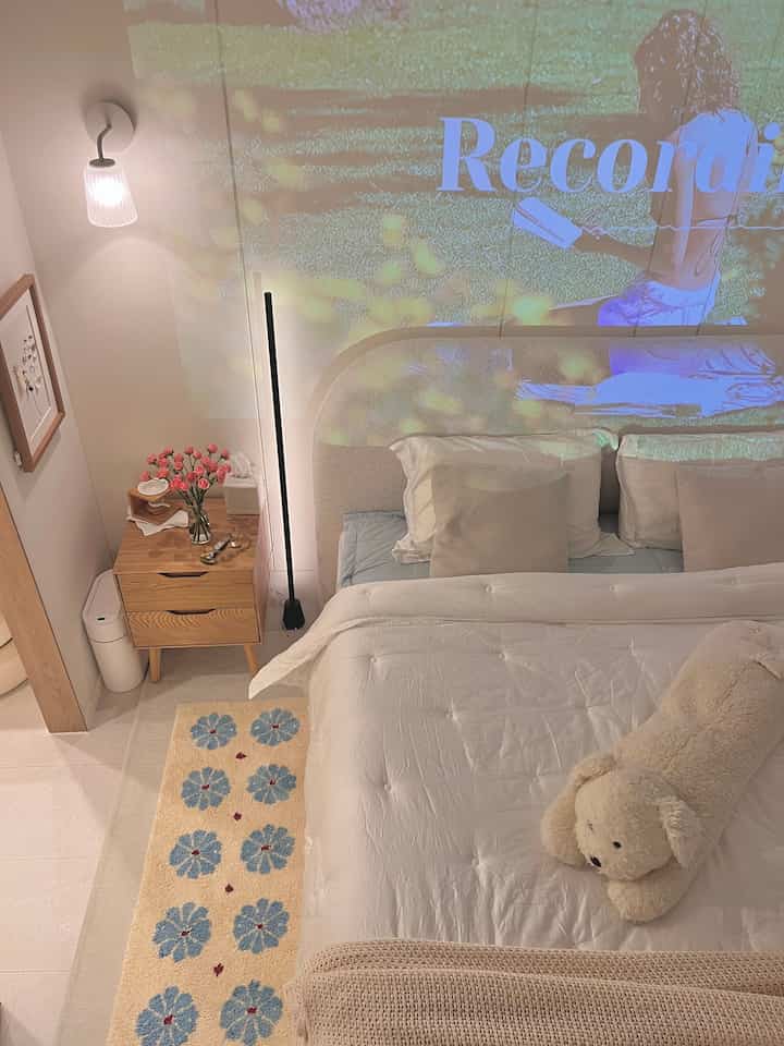 A white and wood tone bedroom featuring a bed with cushions, nightstand with vase, creating a cozy atmosphere