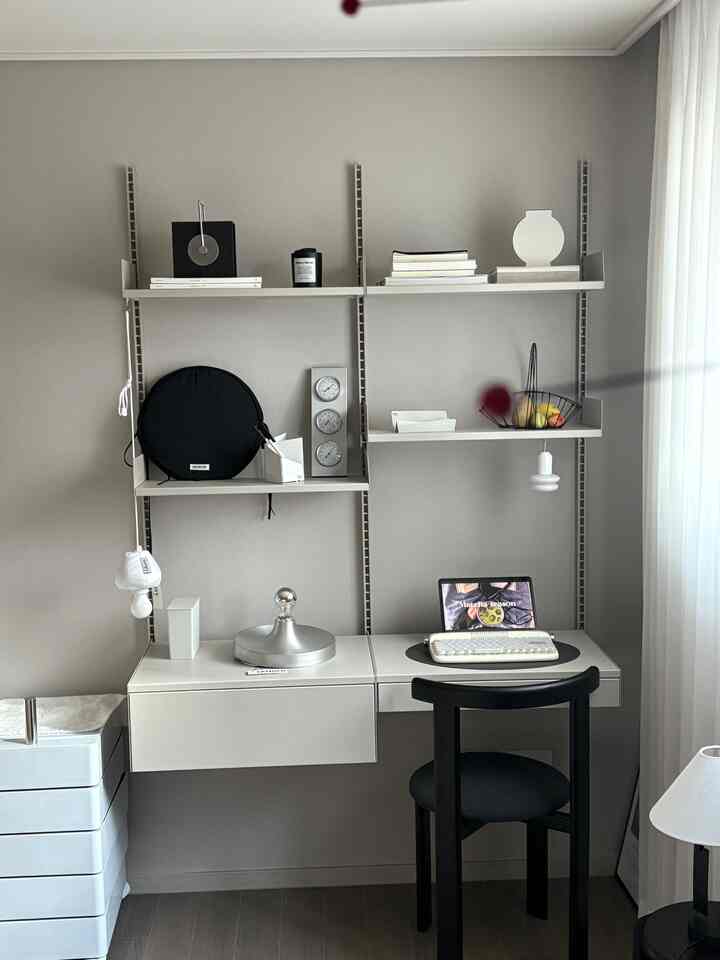 A compact white and black toned home office featuring a wall-mounted desk and chair, arranged with a clean modern design