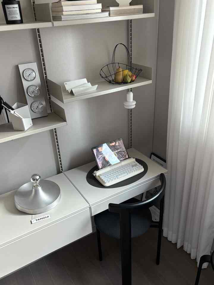Gray-toned compact home office featuring a minimal desk, wall sconce, and organized workspace