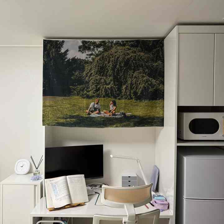 White and beige toned studio apartment home office with fabric poster covering shelf, creating a cozy workspace