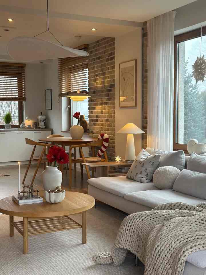 Cozy natural modern living room and dining area with warm wood tones, white curtains, and a cat sitting by the window