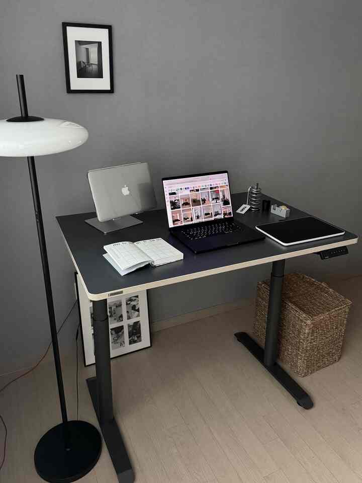 グレーの壁とブラックのスタンディングデスクが配置されたモダンなホームオフィス空間、フロアランプとモノクロの額縁が特徴的なインテリア