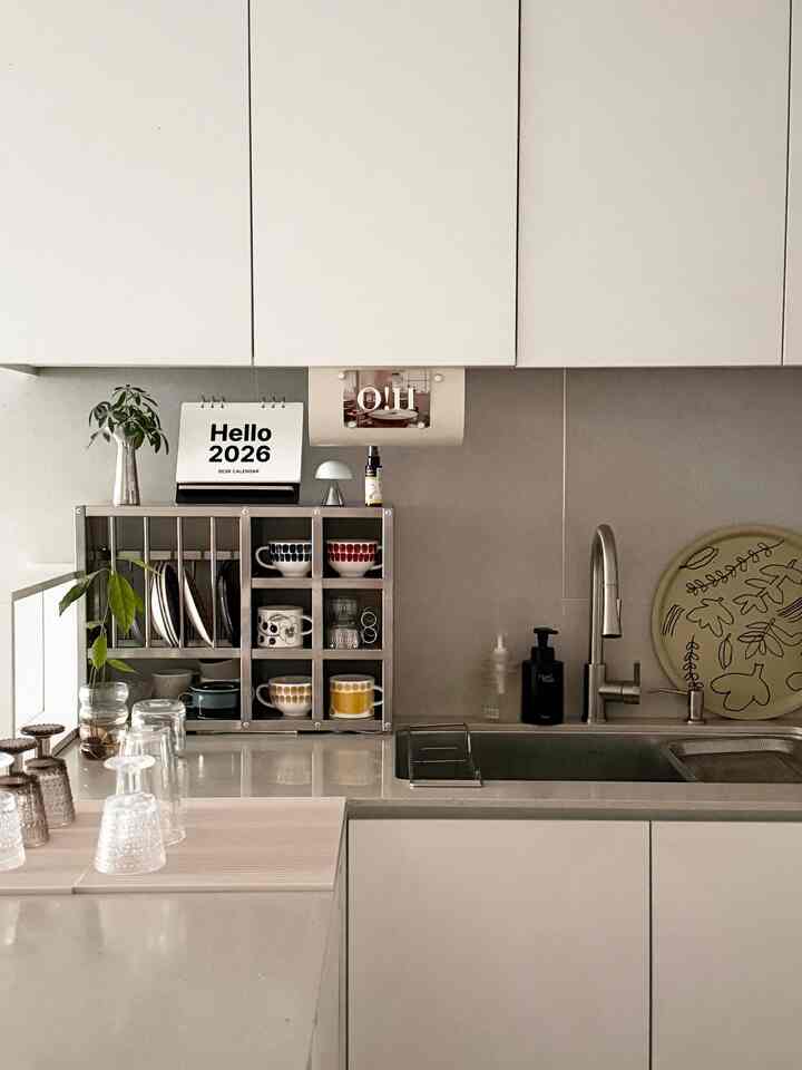 明るい白とベージュのトーンのキッチン、整頓された収納棚とガラス食器、テーブルクロスを配したミニマルでナチュラルな雰囲気のインテリア