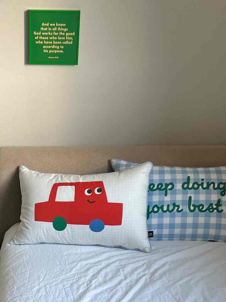 ホワイトの寝具とベージュのベッドが配置されたシンプルな子供部屋、赤い車の柄とチェック柄のキッズピローが置かれた温かみのある空間