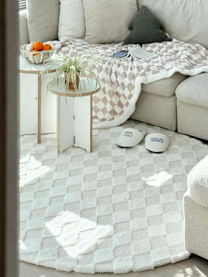 アイボリーとベージュの色調のリビング、快適なソファとチェック柄のブランケット、丸いラグが配置された温かみのある雰囲気の空間