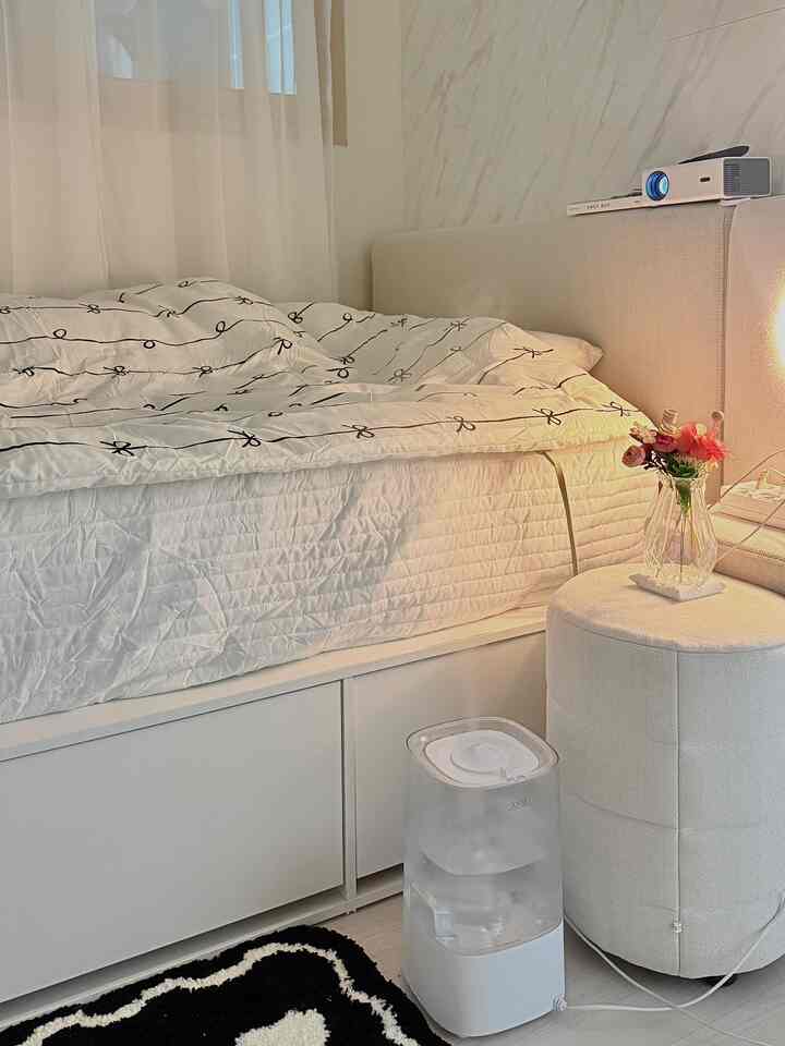 白を基調とした寝室、厚手のキルティングマットレスカバーとベッドカバーが配置された、清潔で温かみのあるインテリア