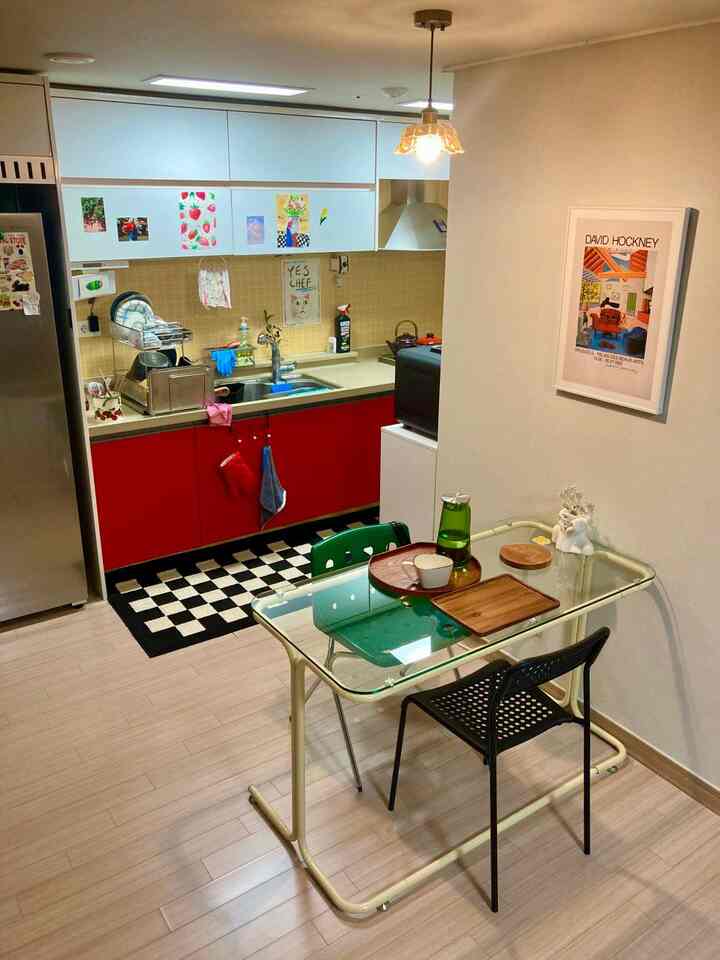 白と赤を基調とした小さなキッチンとダイニングスペース、ガラステーブルとチェッカーボードの床マットが配置された雰囲気のあるインテリア