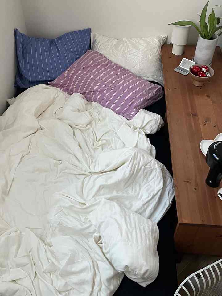 ホワイトとナチュラルな色調の寝室、大きなベッドと枕、木製ナイトテーブル、植物が配置された落ち着いた空間