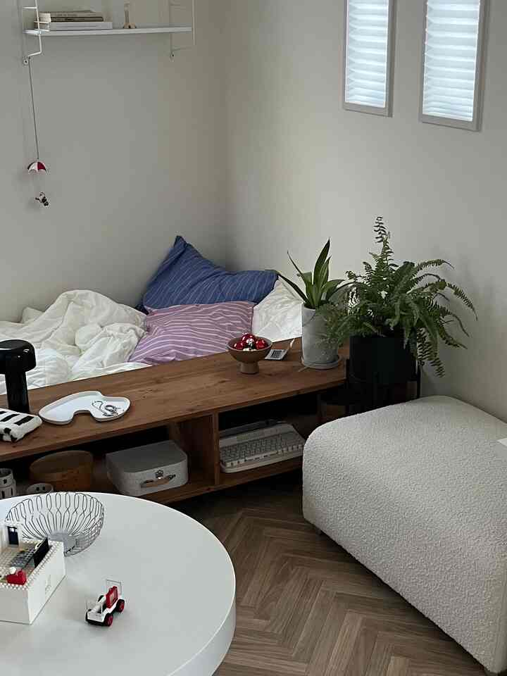 Small bedroom space with white and wood tones featuring a desk and plants in a natural modern style interior