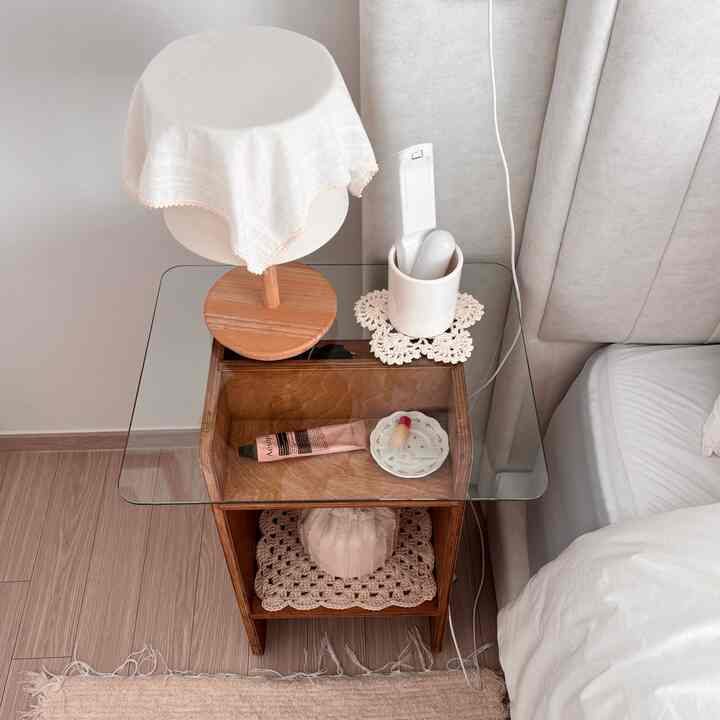 白と茶色のトーンの寝室、木製のサイドテーブルにランプとリモコン収納が配置されたシンプルでナチュラルなインテリア