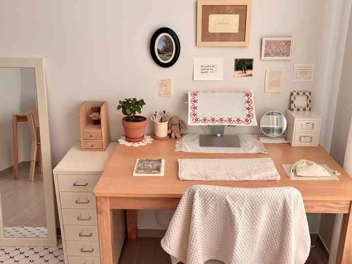 A white and natural wood tone home office space featuring an organized desk with vintage embroidered placemats creating a cozy atmosphere