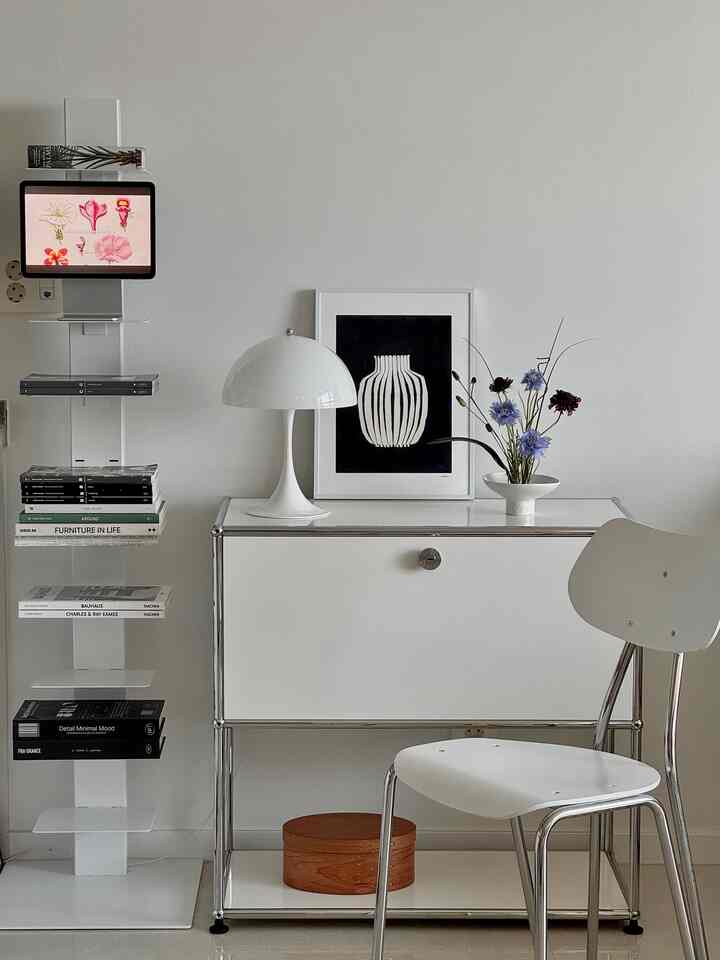 ホワイトとクロームのモダンなリビング、キャビネット、椅子、花瓶、テーブルランプが配置されたシンプルなインテリア