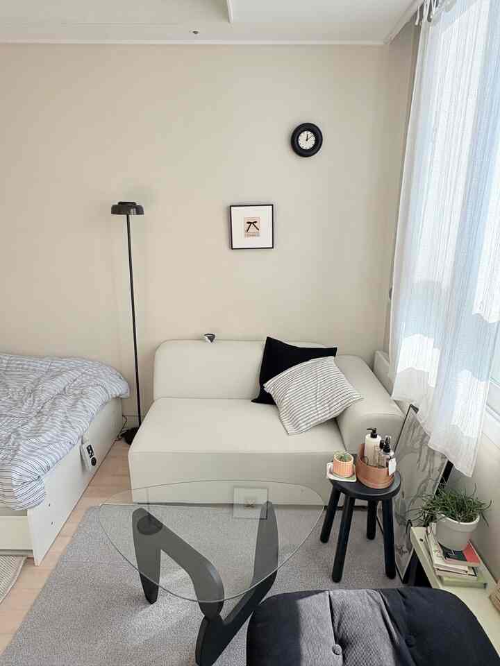 A modern studio living space in white and black tones featuring a sofa, bed, and compact furnishings with a clean, minimal atmosphere