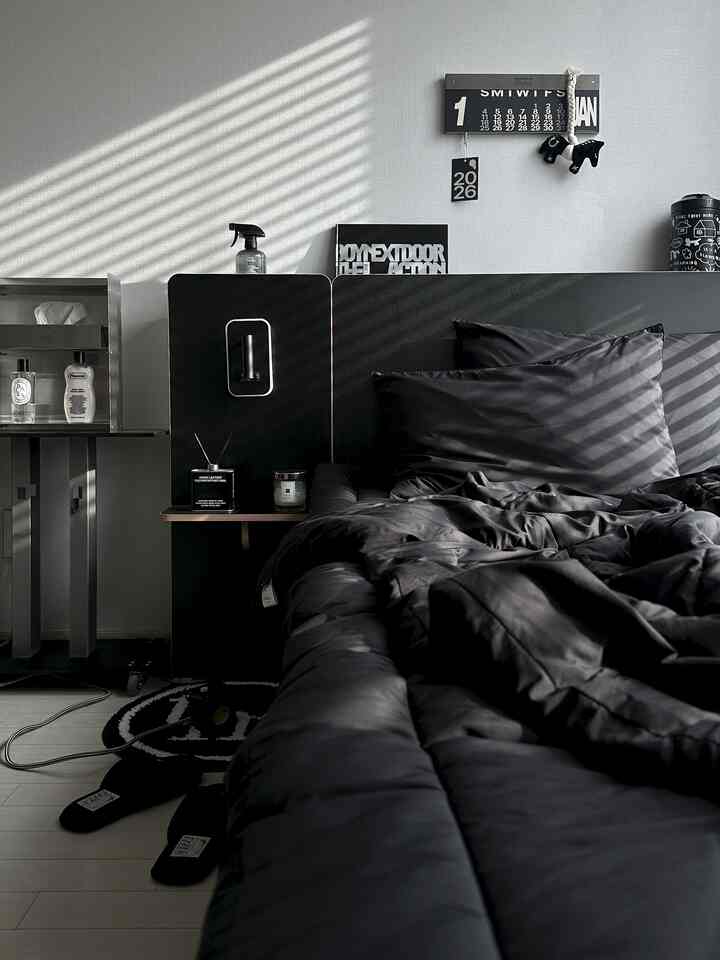 グレーの壁と黒の寝具が調和したモダンな寝室、洗練されたデザインとディフューザーが配置された落ち着いた空間