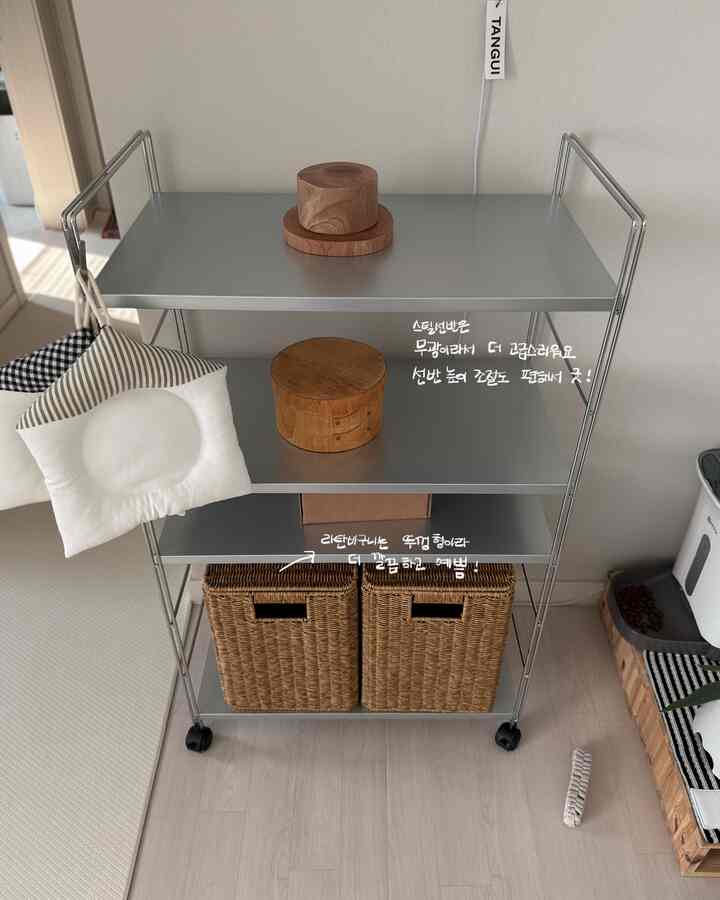 シルバーのスチール棚にナチュラルな木製装飾と蓋付きラタンバスケットが置かれた、整った実用的な収納スペース