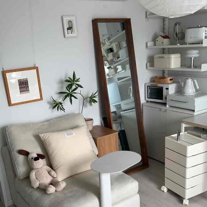 A small living room in white and beige tones featuring a single armchair, side table, wooden framed mirror, reflecting natural modern interior design