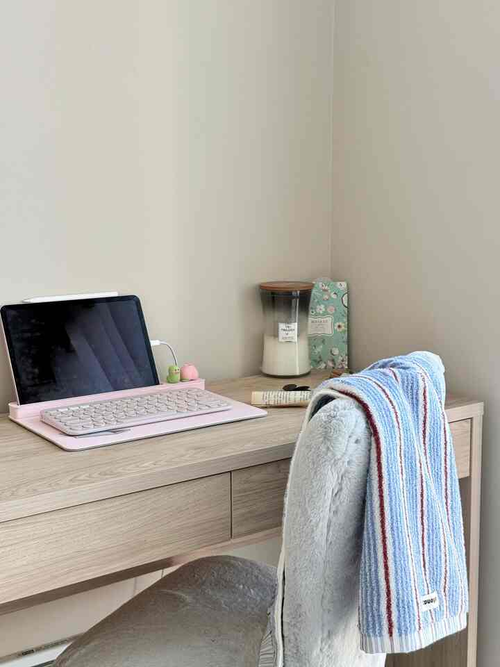 Simple home office desk with light wood tone and sky-blue towel draped over chair