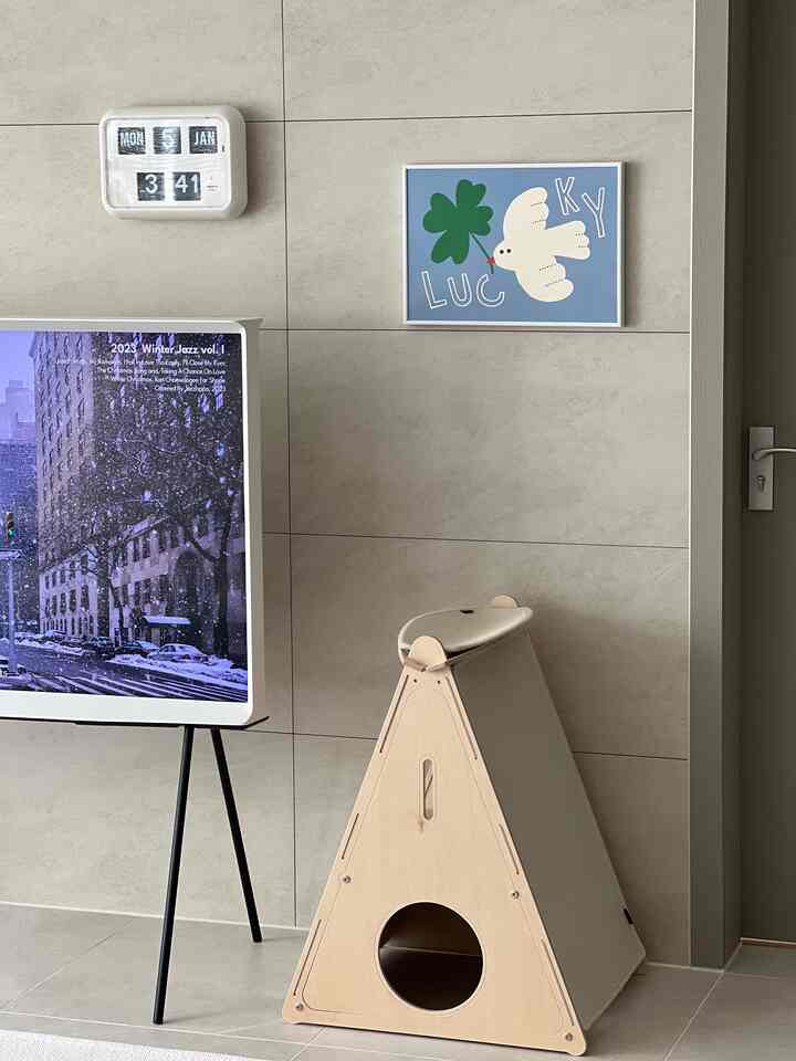 ベージュのタイル壁とナチュラルな木製ペットハウス、壁掛け時計とかわいいポスターが配置されたリビング